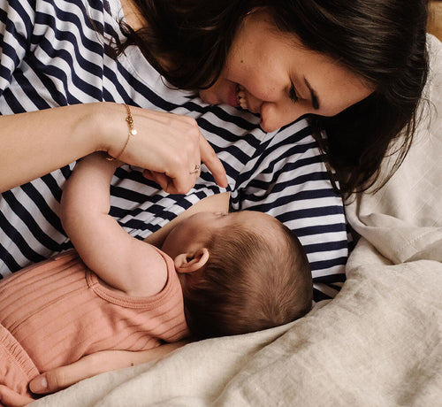 Una mamá y su bebé felices estiradas en la cama mientras le da el pecho - Mustela España - 1