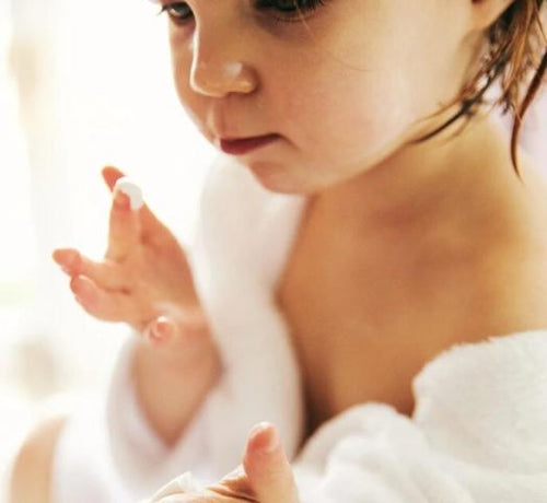 Una bebé recién bañada y con albornoz se aplica crema Mustela en la cara - Mustela España - 1