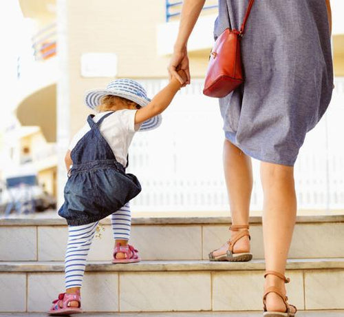 Una niñera y una niña suben unas escaleras mientras se dan la mano - Mustela España - 1