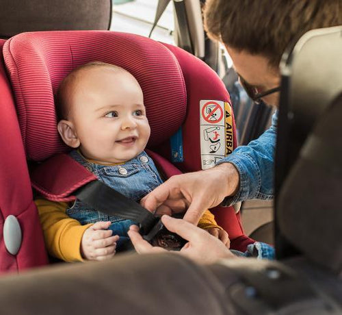 Un bebé contento sentado en la sillita del coche mientras su papá le abrocha el cinturón de seguridad - Mustela España - 1