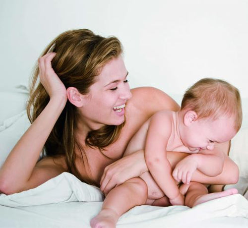 Una mamá y su bebé felices estiradas en la cama después de un baño relajante con jabón Mustela - Mustela España - 1