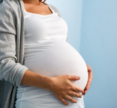 Mujer en una sala de espera para hacerse una prueba del embarazo mientras abraza su tripa con sus manos. - Mustela España - 1