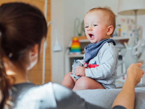 Una mamá de espaldas con su bebé que se encentra sentado y con la boca abierta para hablar. - Mustela España - 1