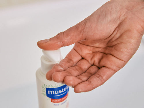 Madre se pone un poco de gel de baño confort en la mano lavar la piel sensible de su bebé. - Mustela España - 5