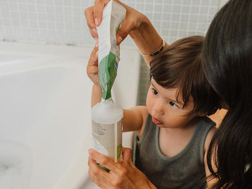 Un niño con su madre está rellenando el envase del gel-champú bio de Mustela con su eco-recarga. slider - Mustela España - 5